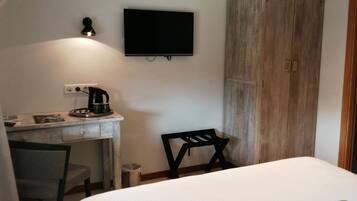 Un dormitorio con cama, escritorio con tetera, silla, televisor y armario.