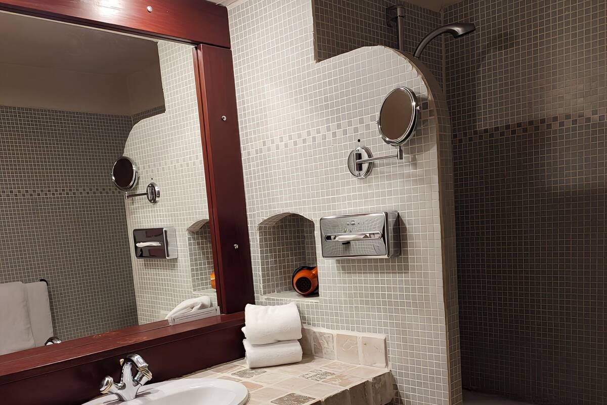 A bathroom with a sink, mirror, towel rack, and shower.