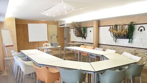 A conference room with multiple tables and chairs, whiteboard, and decorative wall plants.