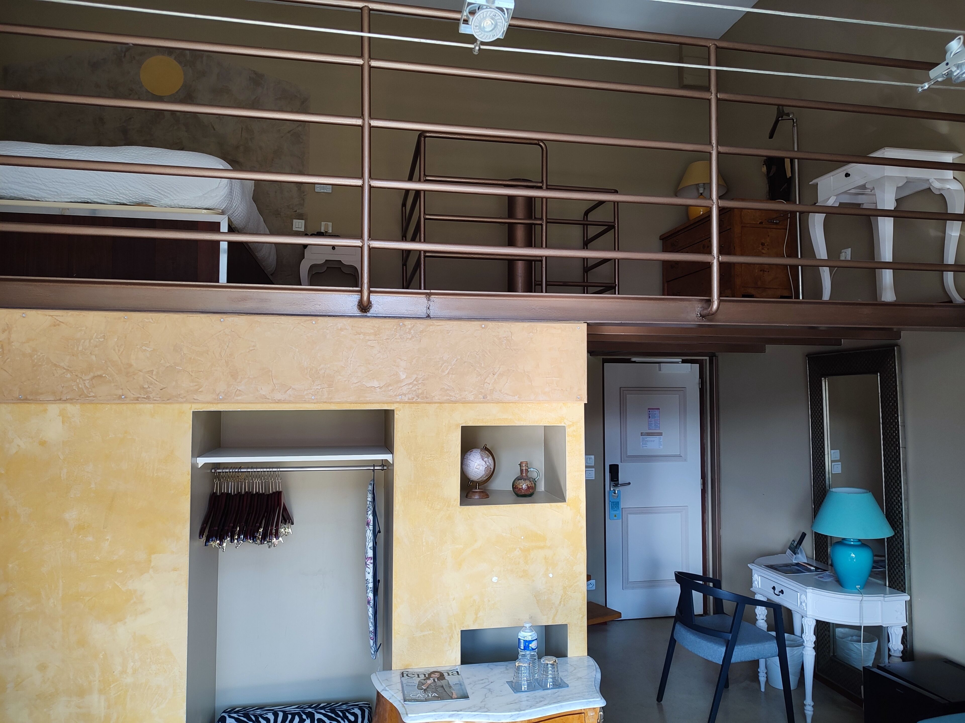 Um quarto com uma cama beliche, uma mesinha com abajur, uma cadeira e uma porta.