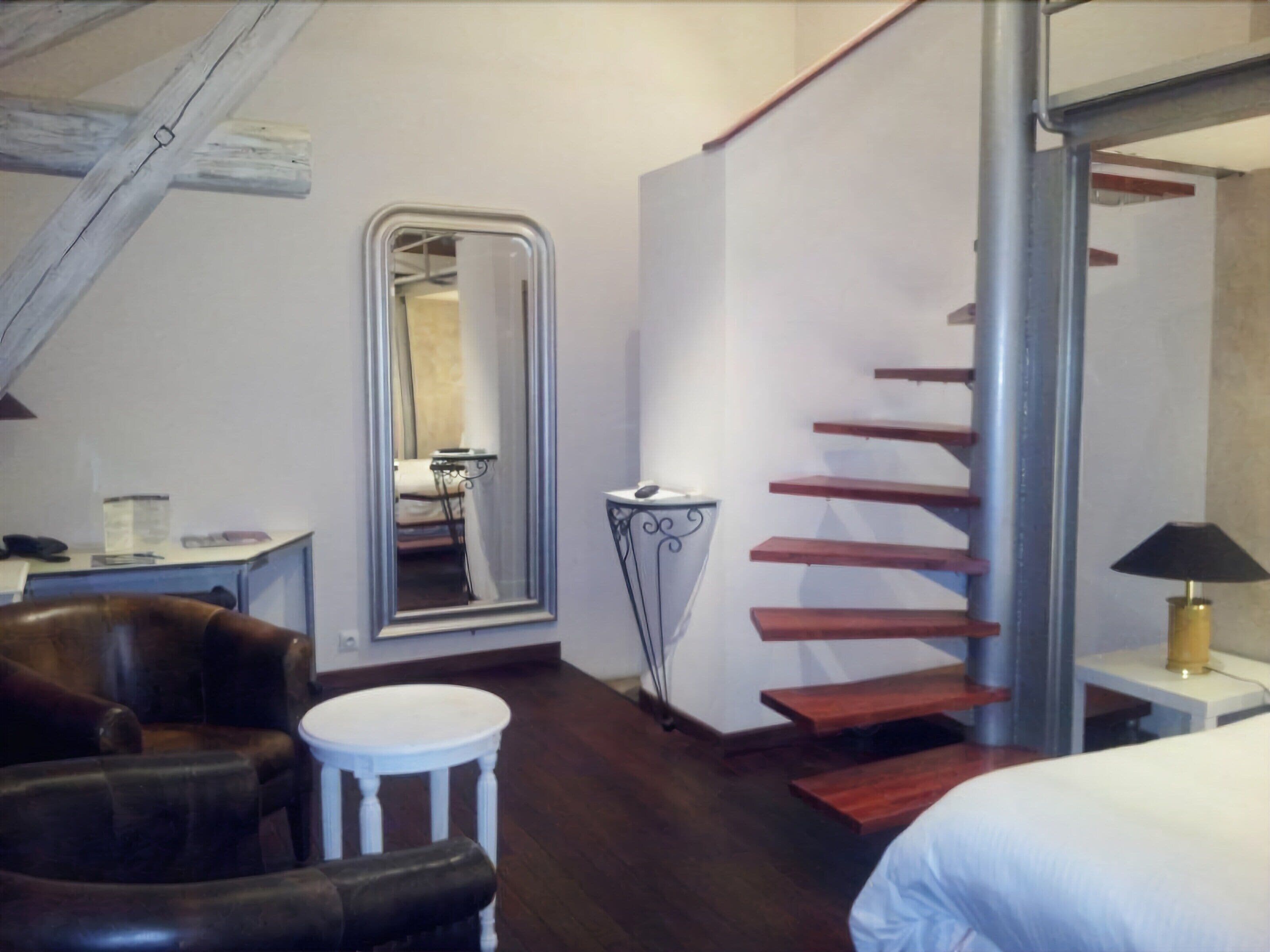 Un dormitorio con escalera de madera, un espejo grande, una mesita redonda y una cama.