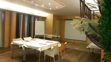 Une salle de conférence avec une table blanche, des chaises, un projecteur et un tableau blanc.
