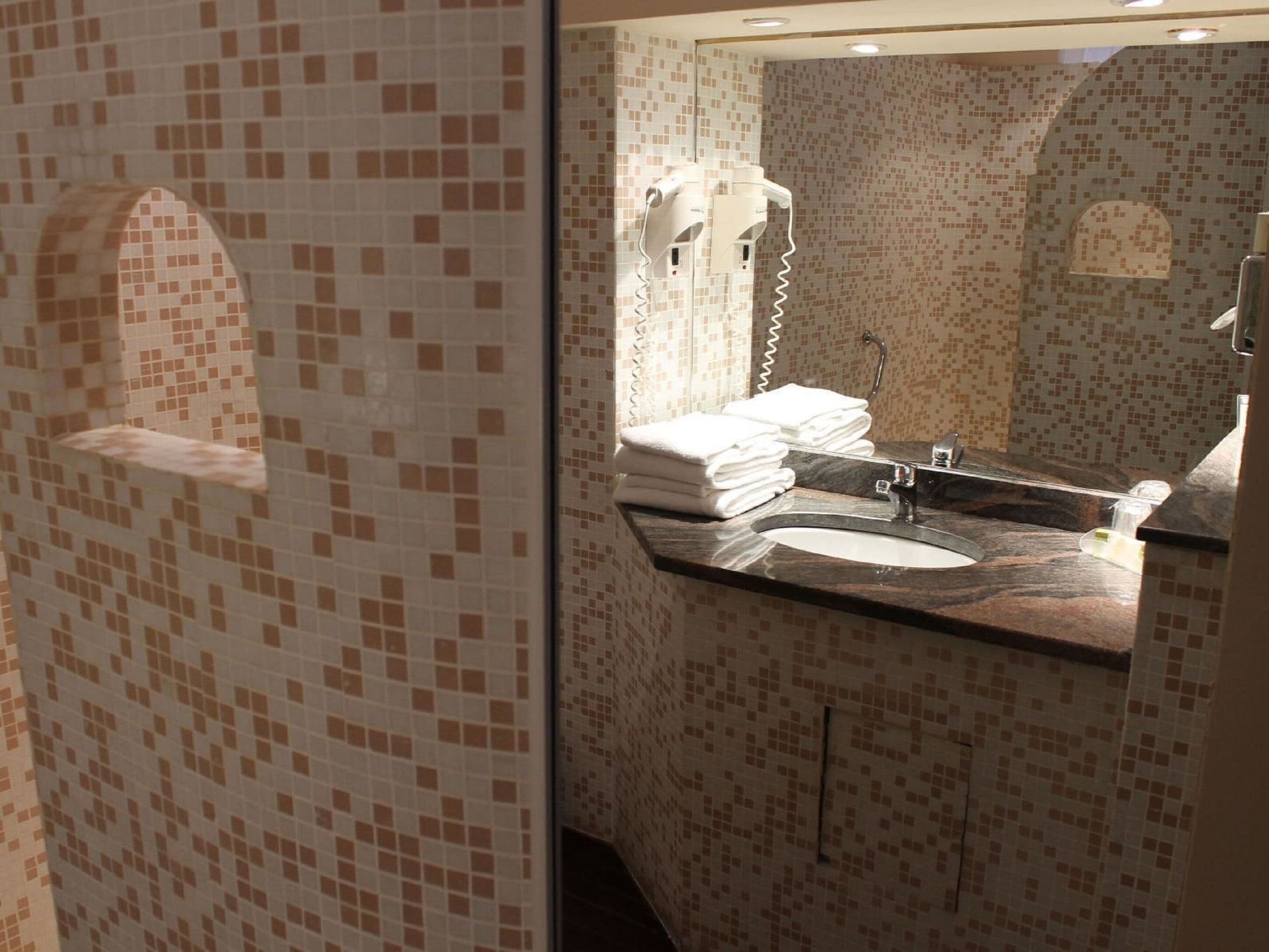 A bathroom with a tiled mosaic wall, a sink with a mirror, and a hairdryer.