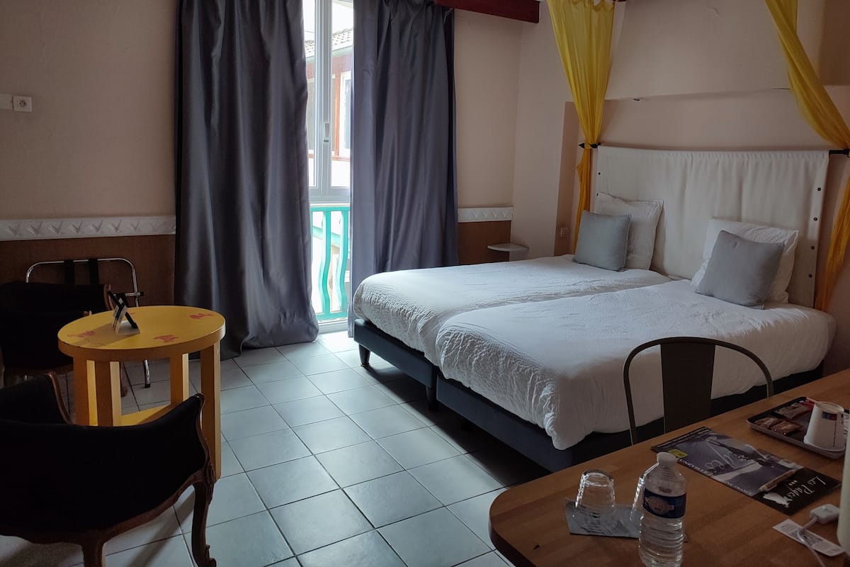 A hotel room with a bed, a small table, a chair, and a window with curtains.
