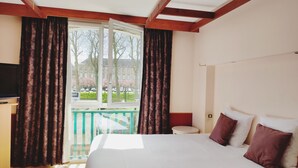 A hotel room with a large bed, a television, and a balcony with curtains.