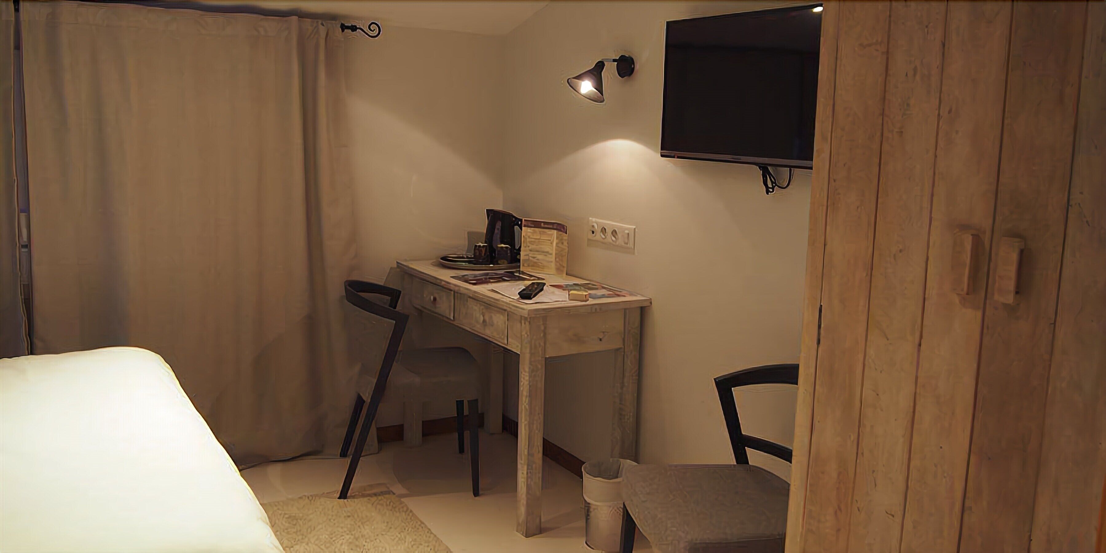Ein kleiner, gemütlicher Raum mit einem Bett, einem Schreibtisch, einem Stuhl und einem an der Wand befestigten Fernseher.