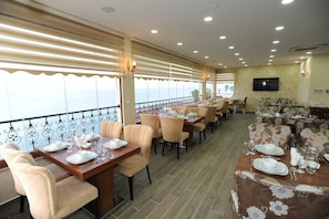 En restaurang med bord uppdukade för middag, en stor TV-skärm på väggen och utsikt över havet genom fönstren.