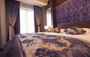 A hotel room with a large bed, dark curtains, a tufted headboard, and a patterned bedspread. - Vurna Butik Hotel (Akçaabat)