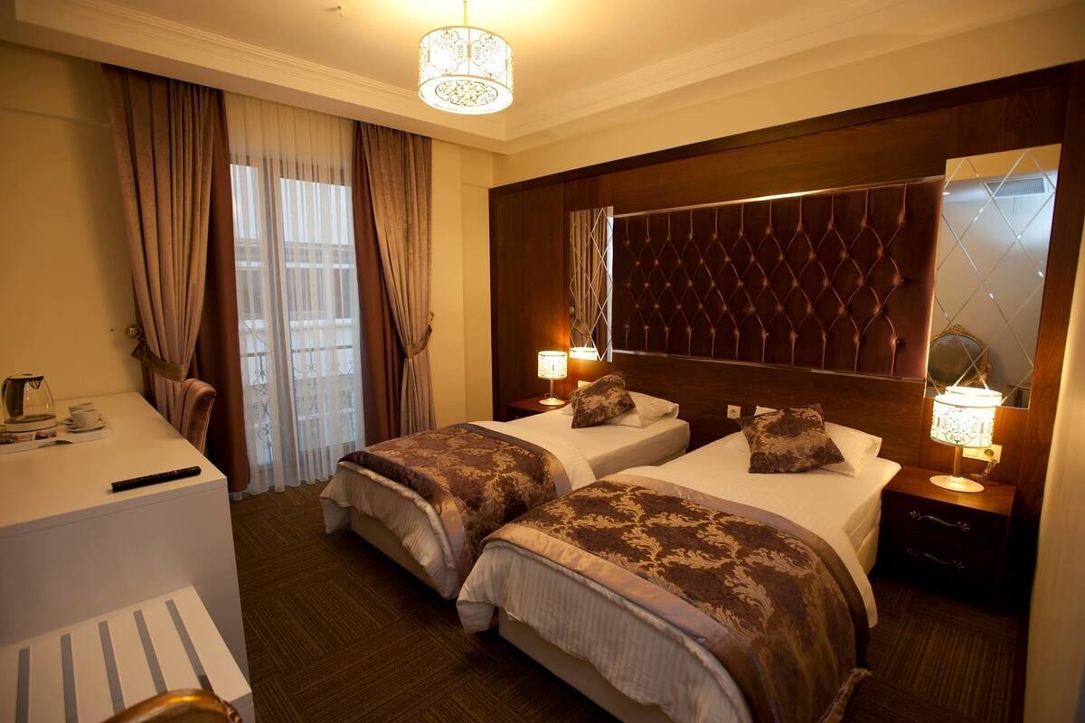 Una camera d'albergo con due letti, una scrivania, una sedia, uno specchio grande e un lampadario.