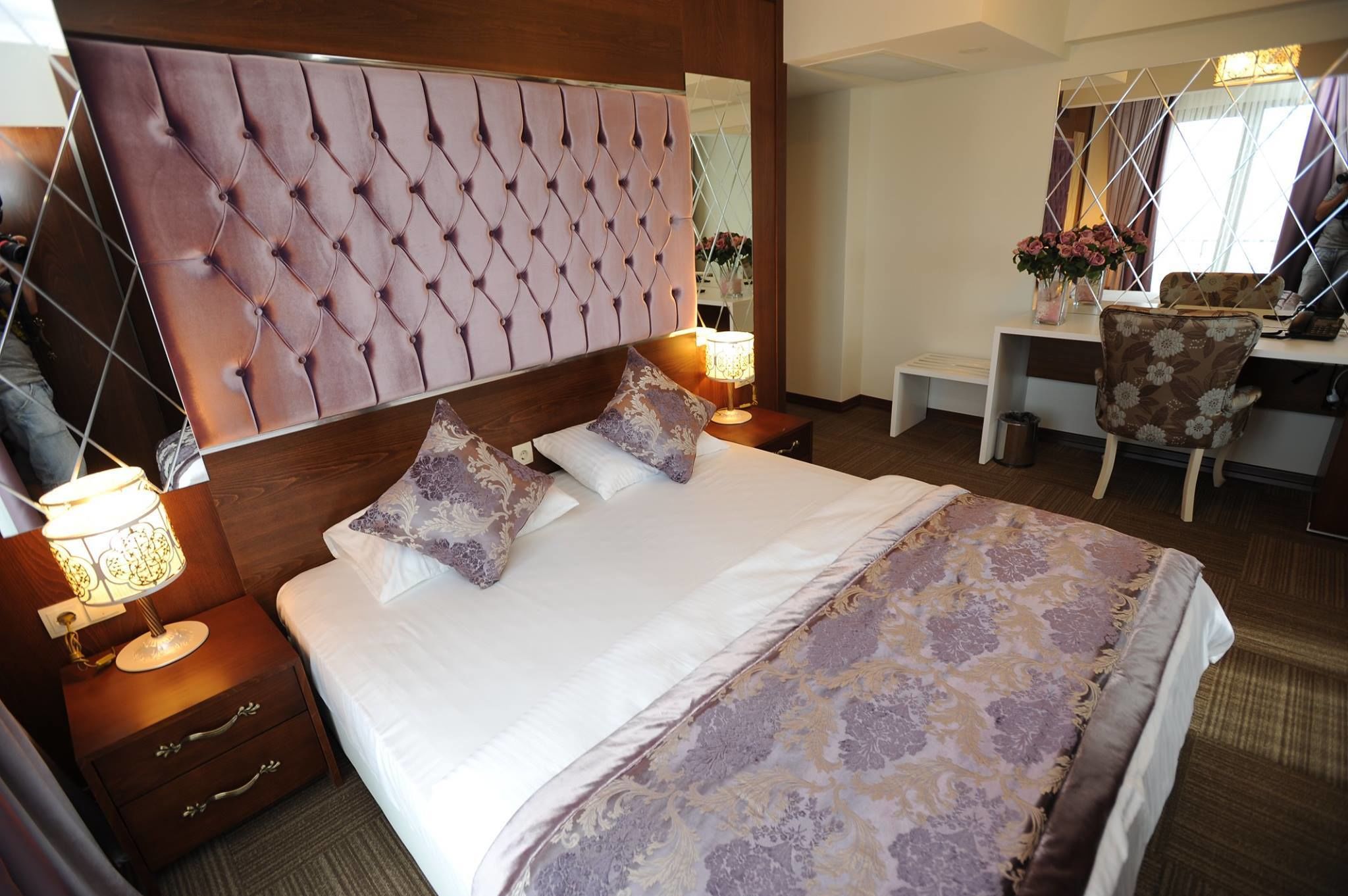 A hotel room with a large bed, a wooden headboard, a desk with a chair, and a mirror.