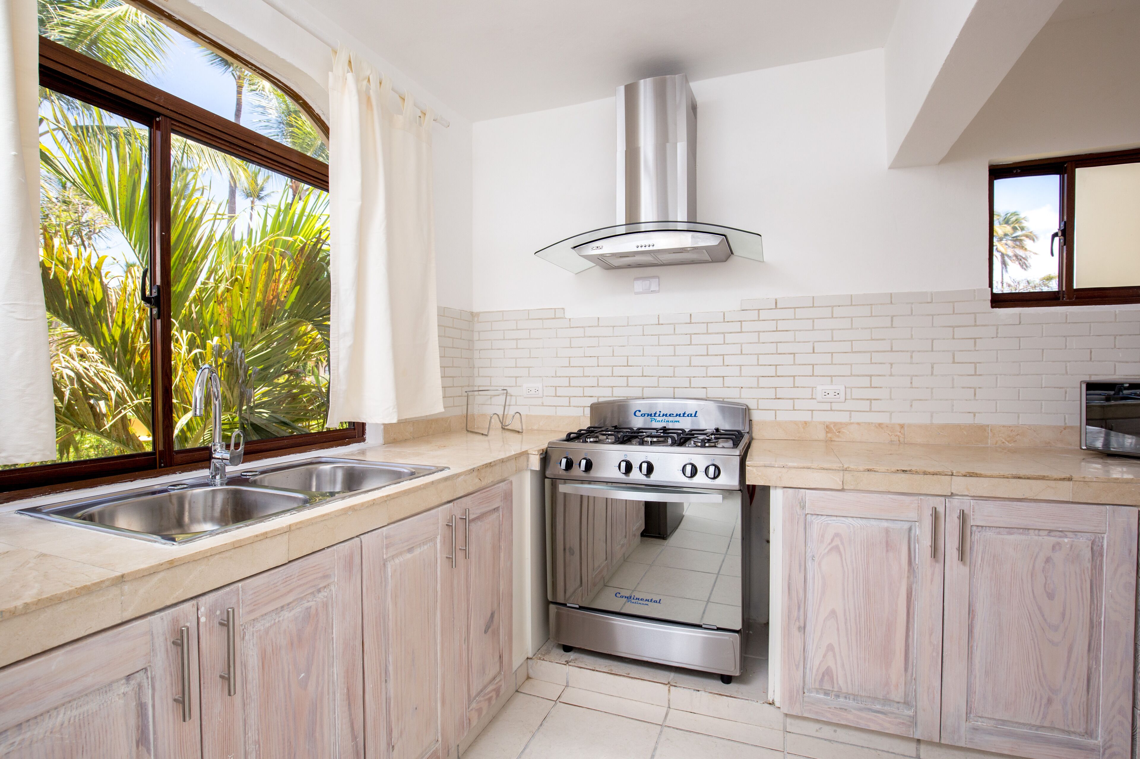 A kitchen with a gas stove, stainless steel sink, and white tiled backsplash.