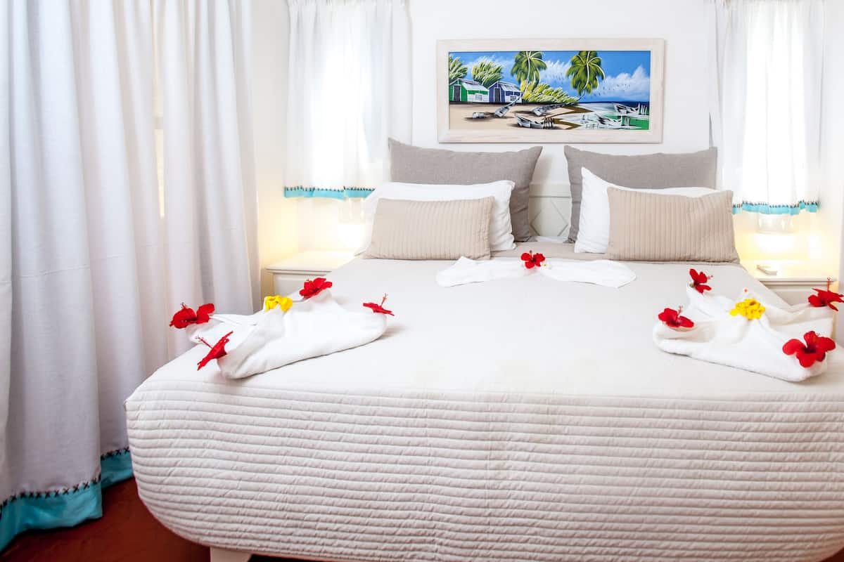 A hotel room with a large bed, two bedside tables, a painting on the wall, and a wardrobe.