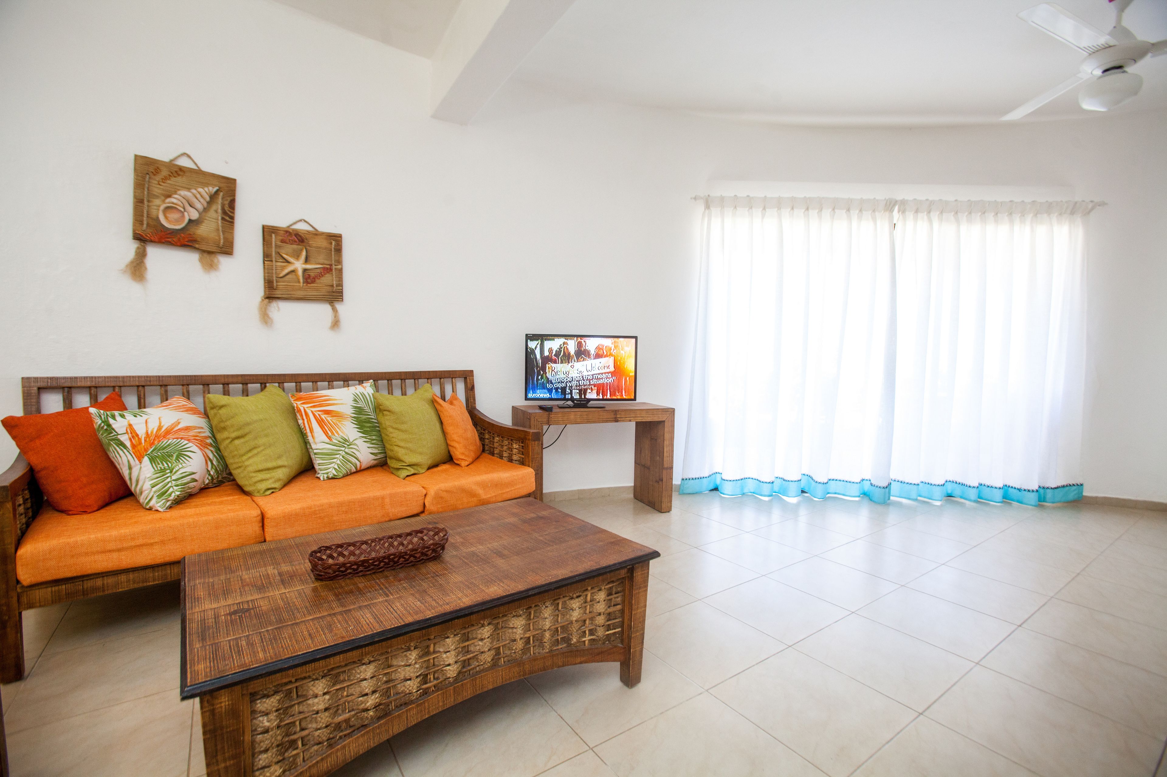 Una sala de estar con un sofá de madera, una mesa de centro y un televisor sobre un mueble de madera.