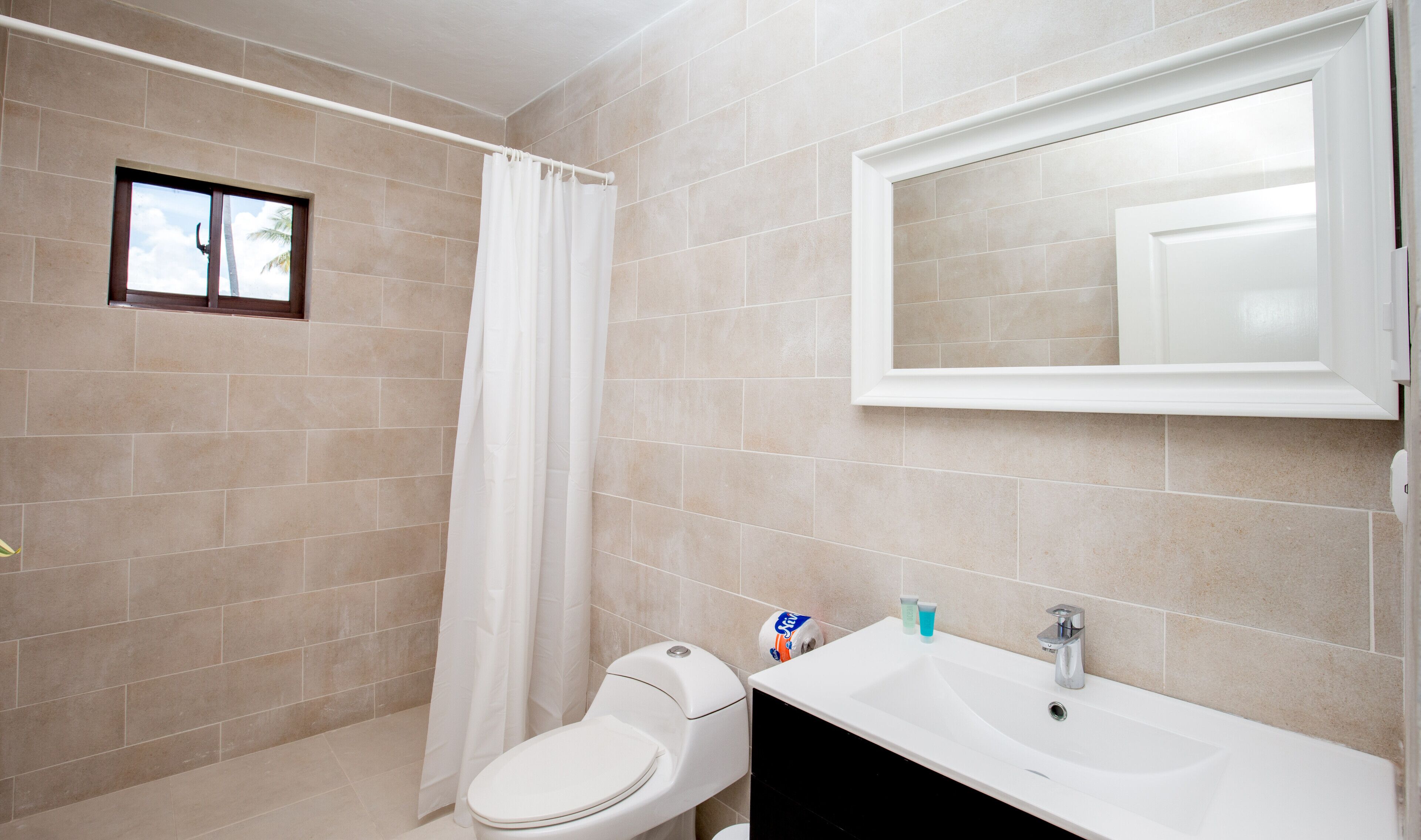 A bathroom with beige tiles, a white toilet, a sink, and a mirror.