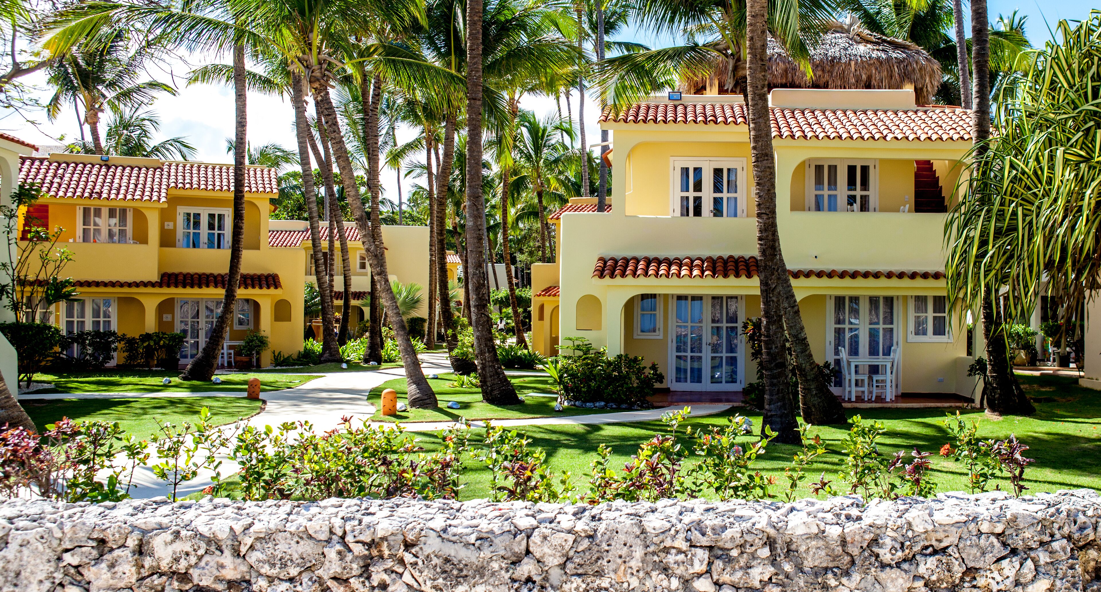 A resort with yellow buildings, palm trees, and a stone wall.