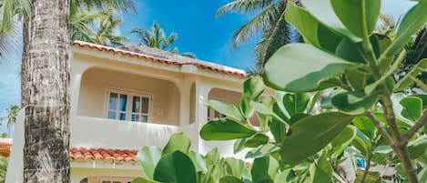 A building with a tiled roof and arched windows, surrounded by palm trees and greenery.