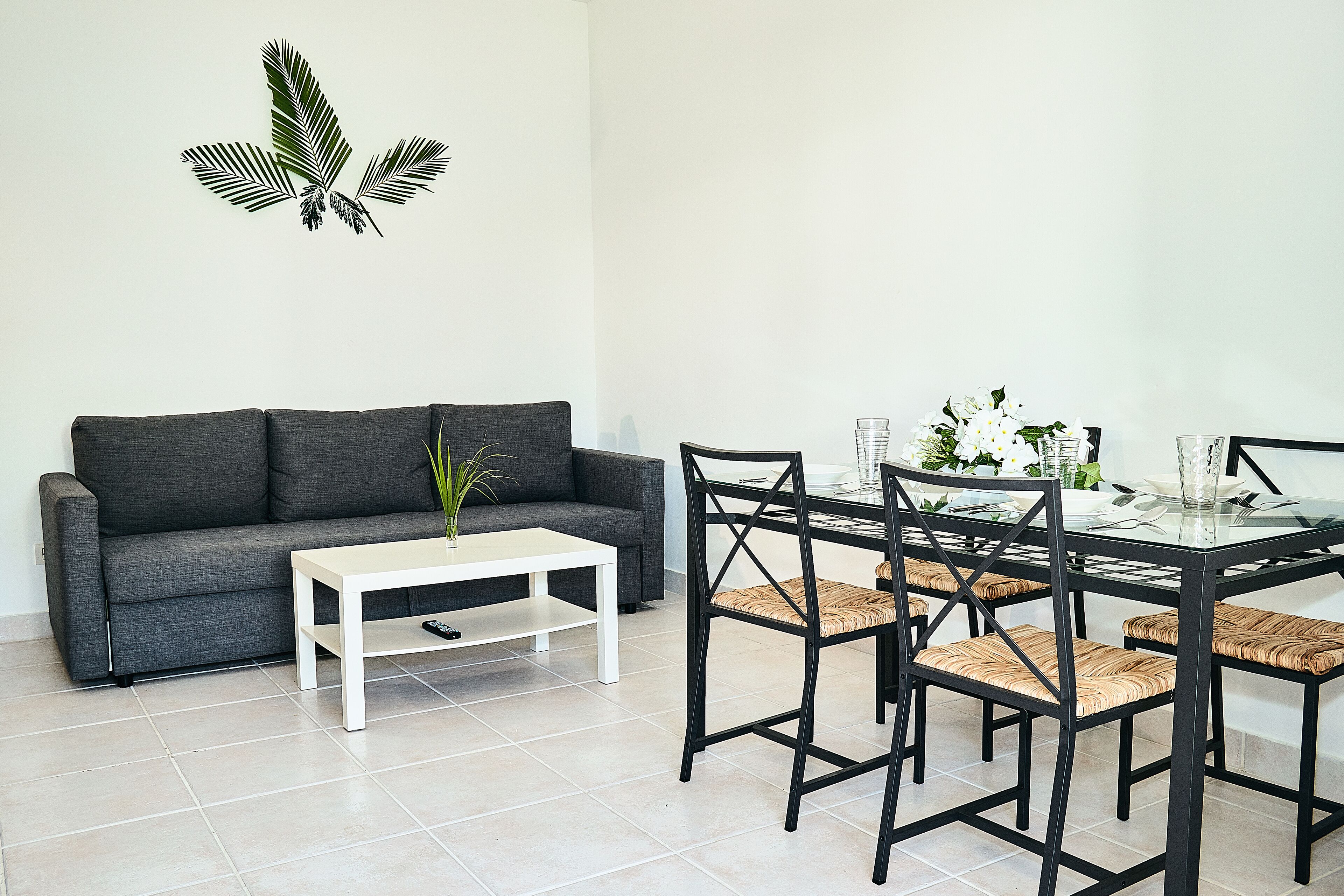 A modern living room with a grey sofa, a white coffee table, and a glass-top dining table with black chairs.