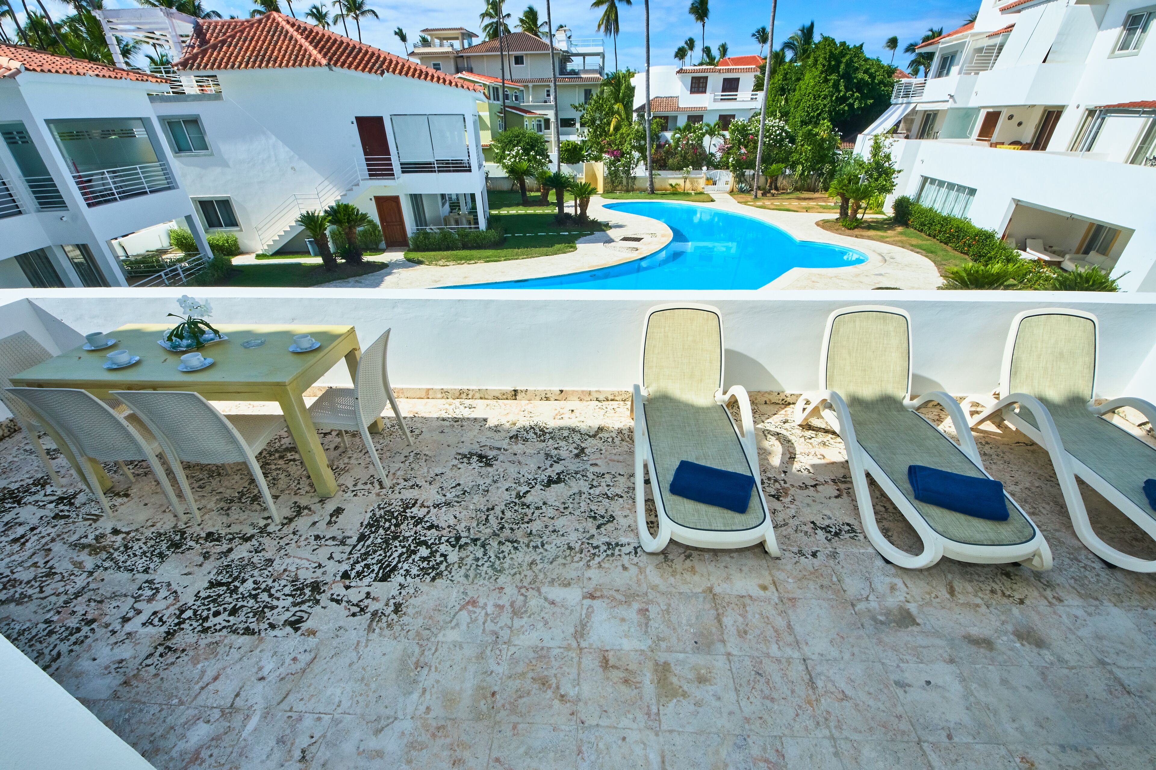 A poolside area with a table and chairs, a pool, and modern buildings in the background.