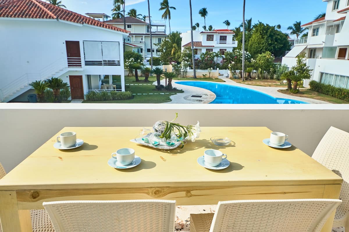 A table with four white cups and saucers, a decorative tray with flowers, and wicker chairs.
