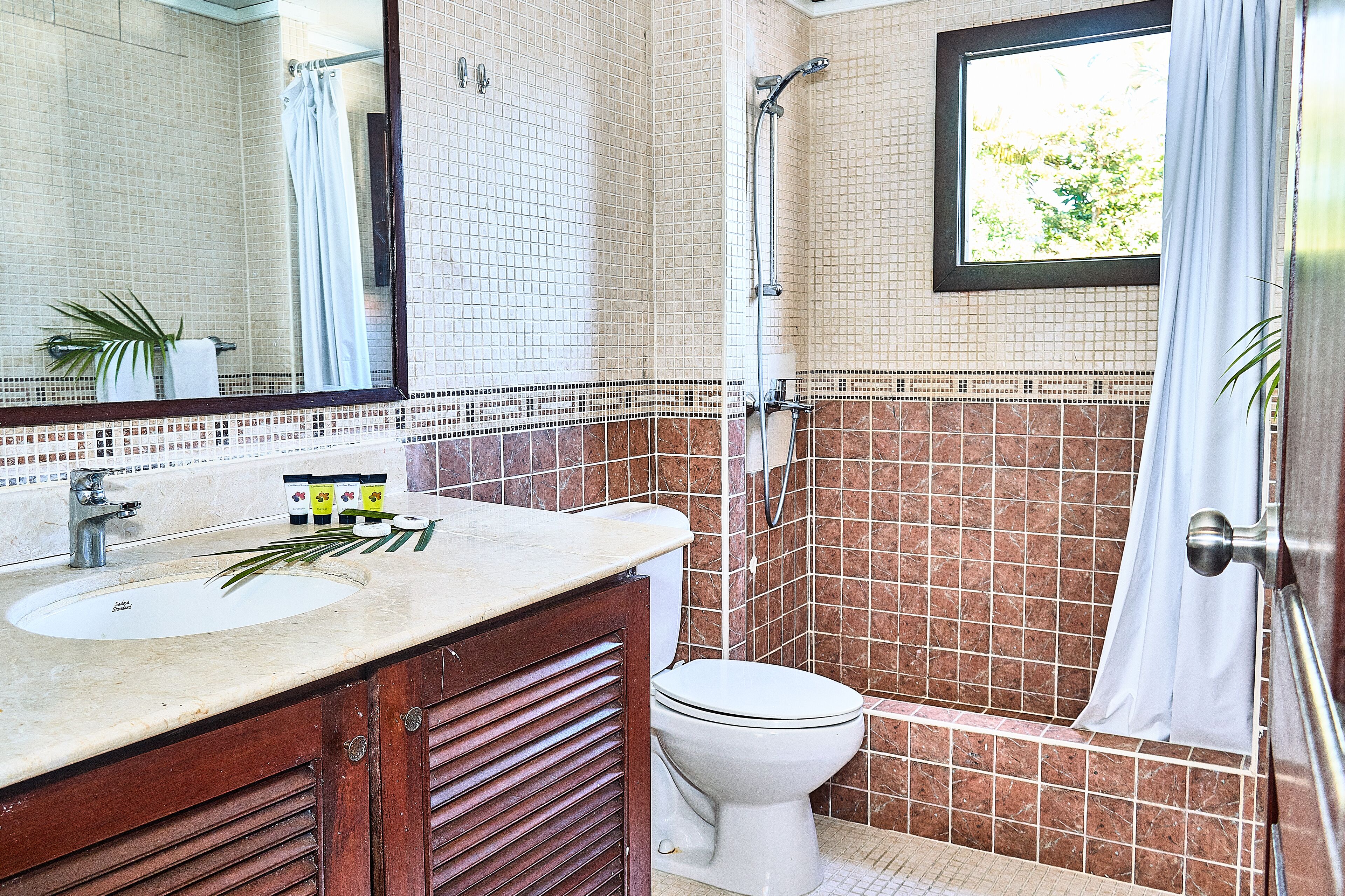 A bathroom with a sink, mirror, toilet, shower, and tiled walls.