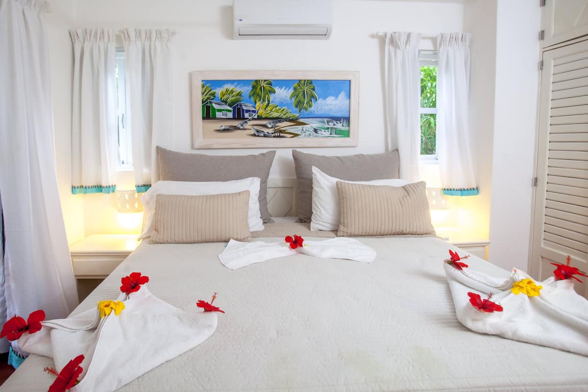 A hotel room with a bed, pillows, a painting of a beach scene, and a window with curtains.