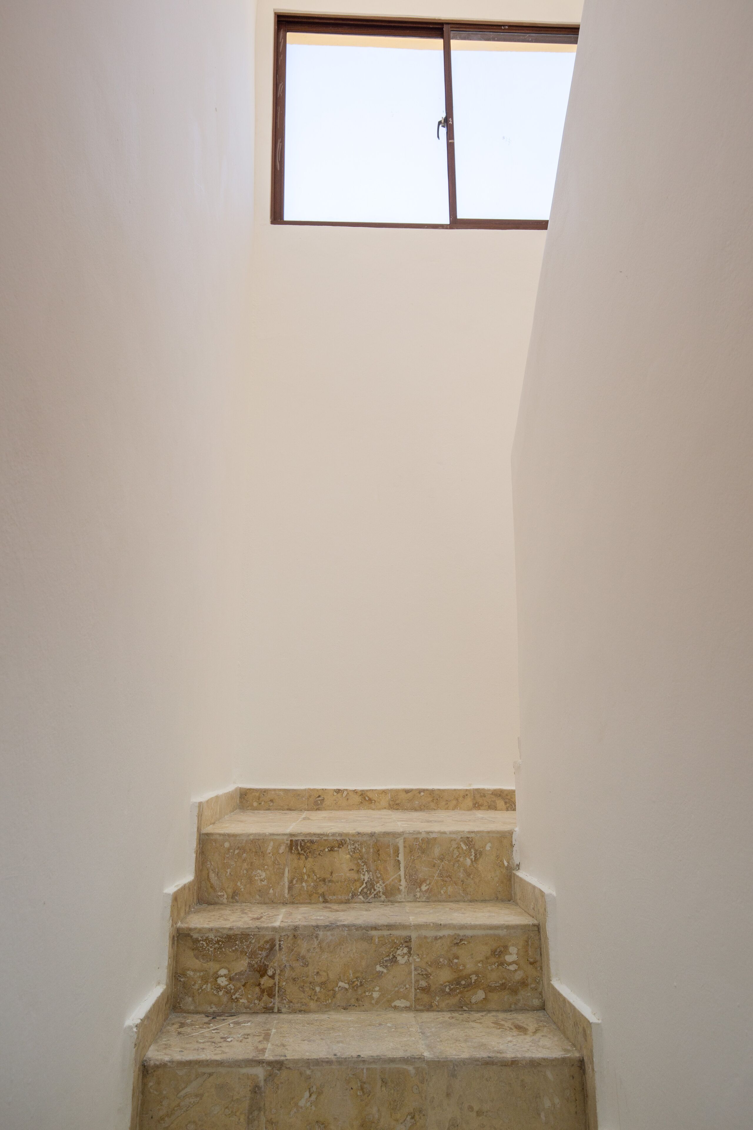 A set of beige stone steps leading up to a window with a wooden frame.