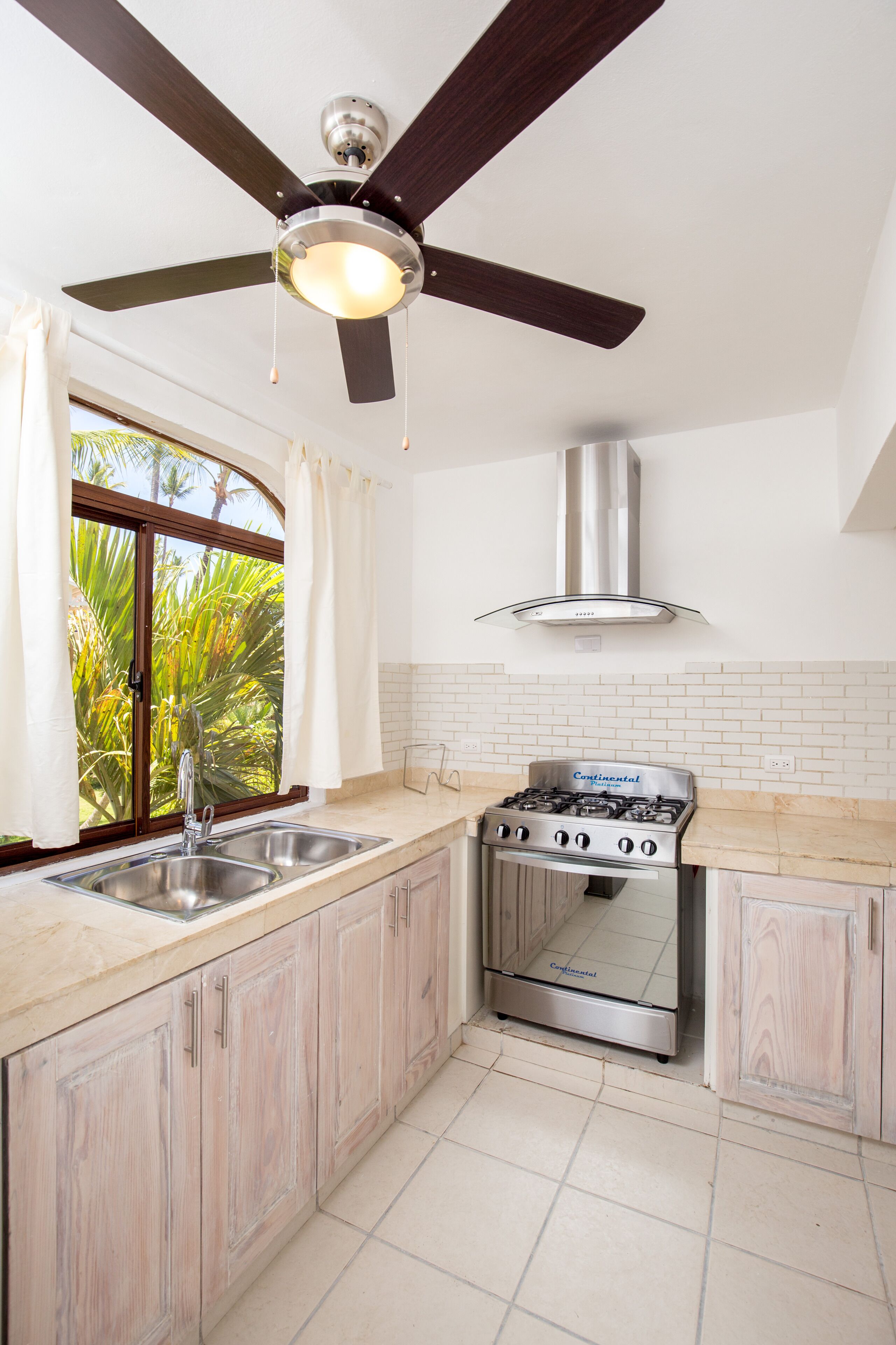 A kitchen with a stove, sink, and ceiling fan.