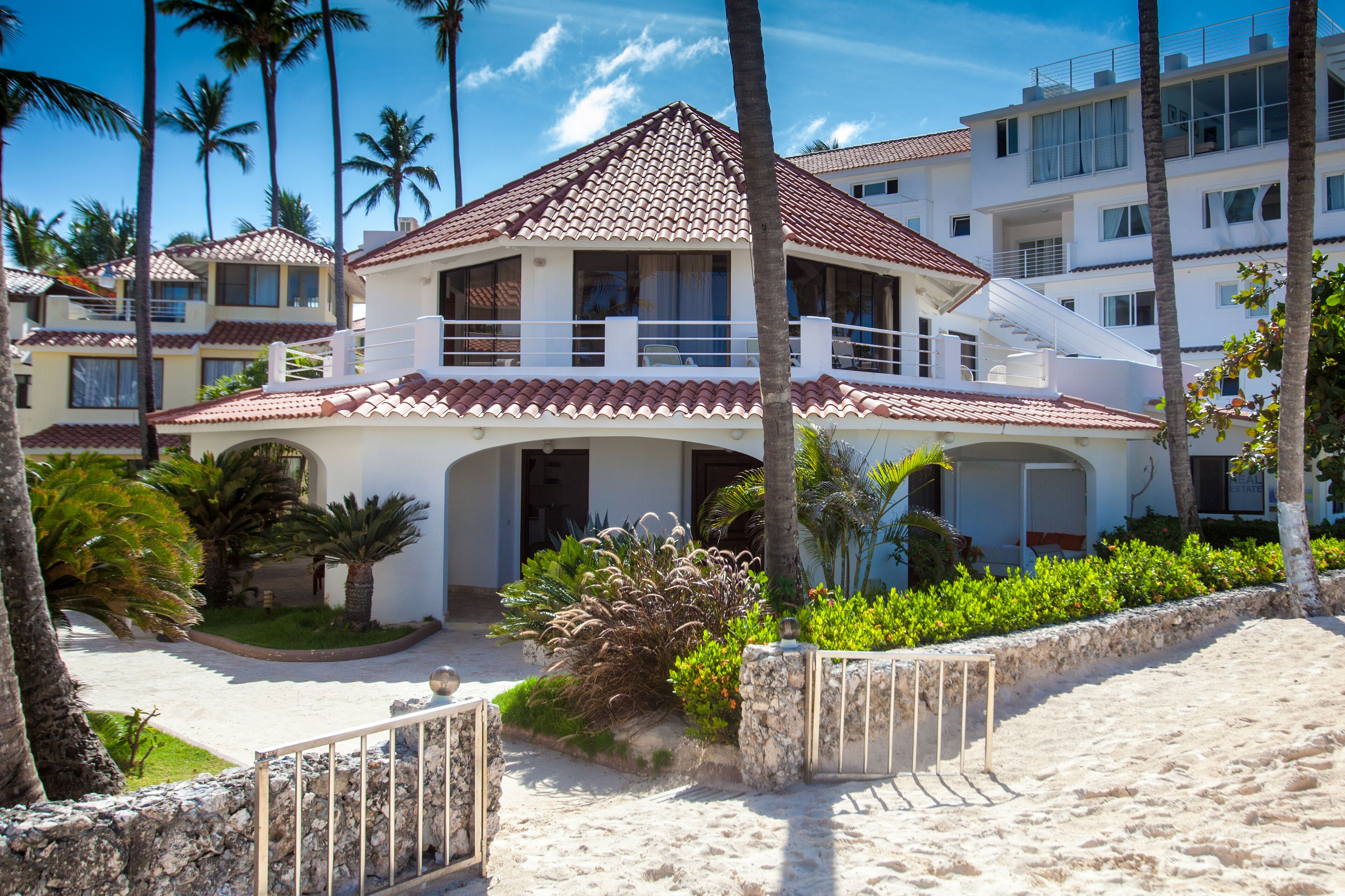 A beachfront hotel with a red-tiled roof, multiple balconies, and a sandy beach area.