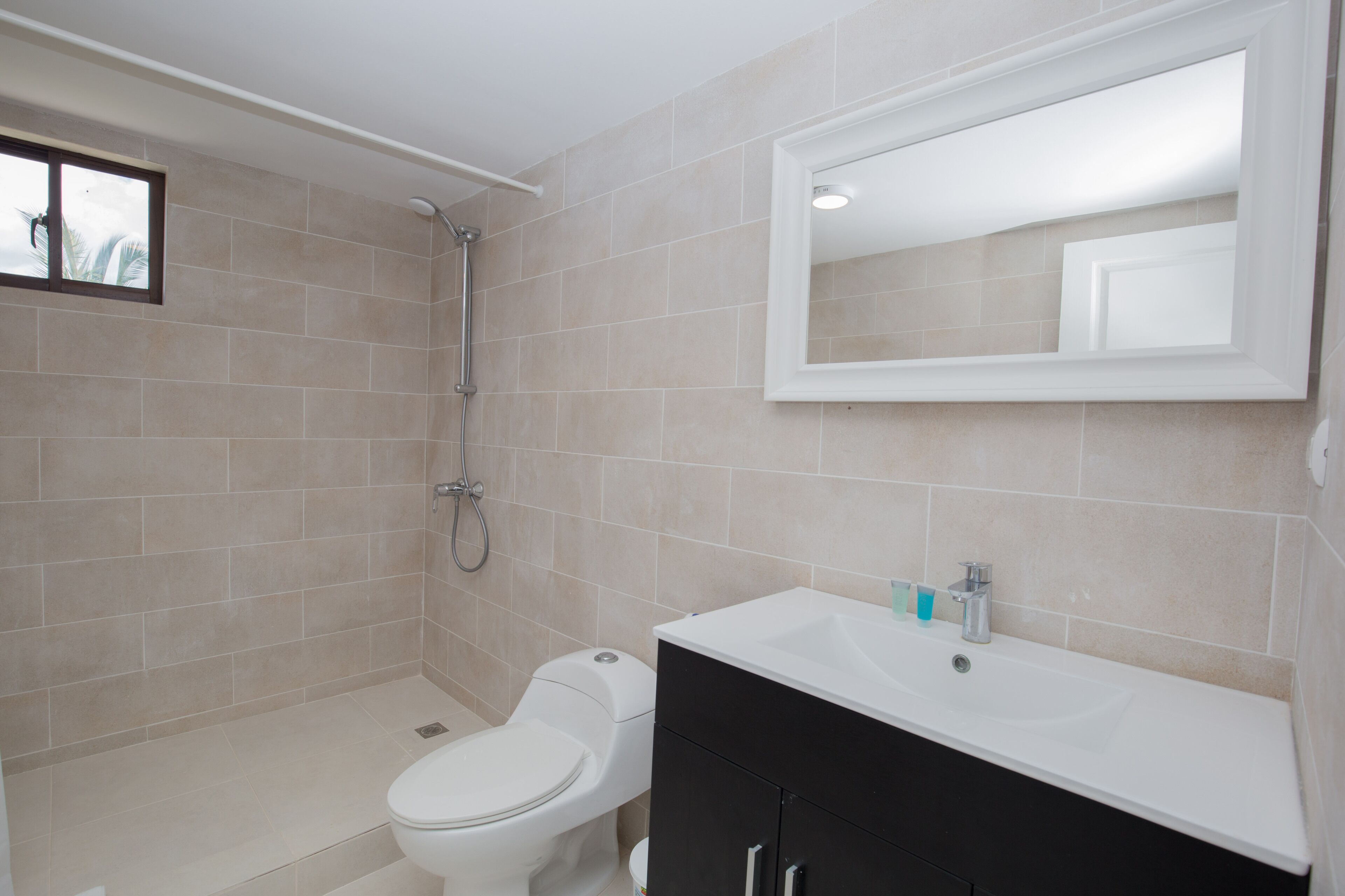 A bathroom with beige tiles, a white toilet, a black cabinet, and a white sink.