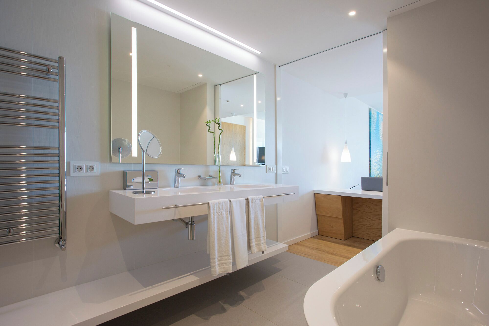 A modern bathroom with a large mirror, two sinks, a bathtub, and a towel rack.