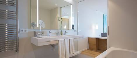 A modern bathroom with a large mirror, two sinks, a bathtub, and a towel rack.
