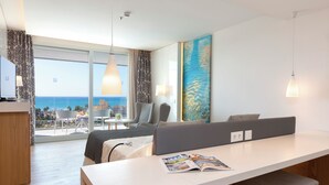 A modern hotel room with a large window, a dining area, a sofa, and a desk with a magazine.