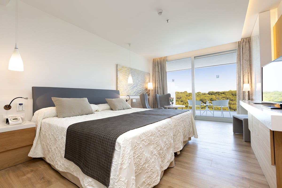 Une chambre moderne avec un grand lit, des tables de chevet, un bureau et une vue sur l’extérieur.