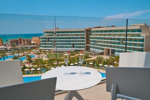 Ein Hotelbalkon mit Pool, Liegestühlen und Blick auf das Meer und die Hotelgebäude.