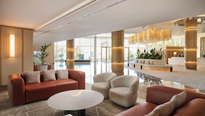 A spacious lobby with leather sofas, a coffee table, and a reception area with a desk and chairs.
