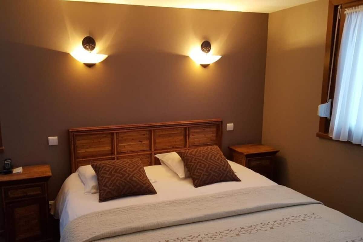 A hotel room with a wooden headboard, two bedside lamps, a bed with white linens and patterned pillows, and a window with curtains.