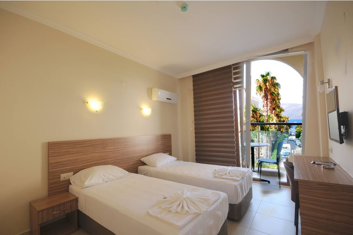 A hotel room with two beds, a desk, and a balcony with a view.