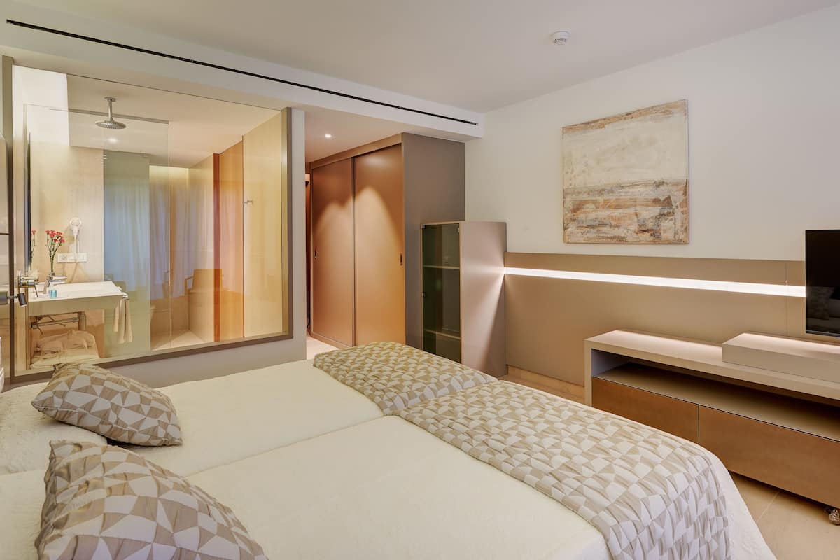 Quarto de hotel moderno com uma cama grande, escrivaninha com TV de tela plana, closet espaçoso e banheiro com box de vidro.