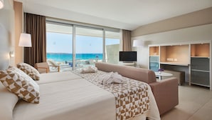 A hotel room with a bed, a sofa, a TV, and a desk. There is a view of the beach and the ocean through large windows. - Hipotels Gran Playa de Palma (Palma de Mallorca)