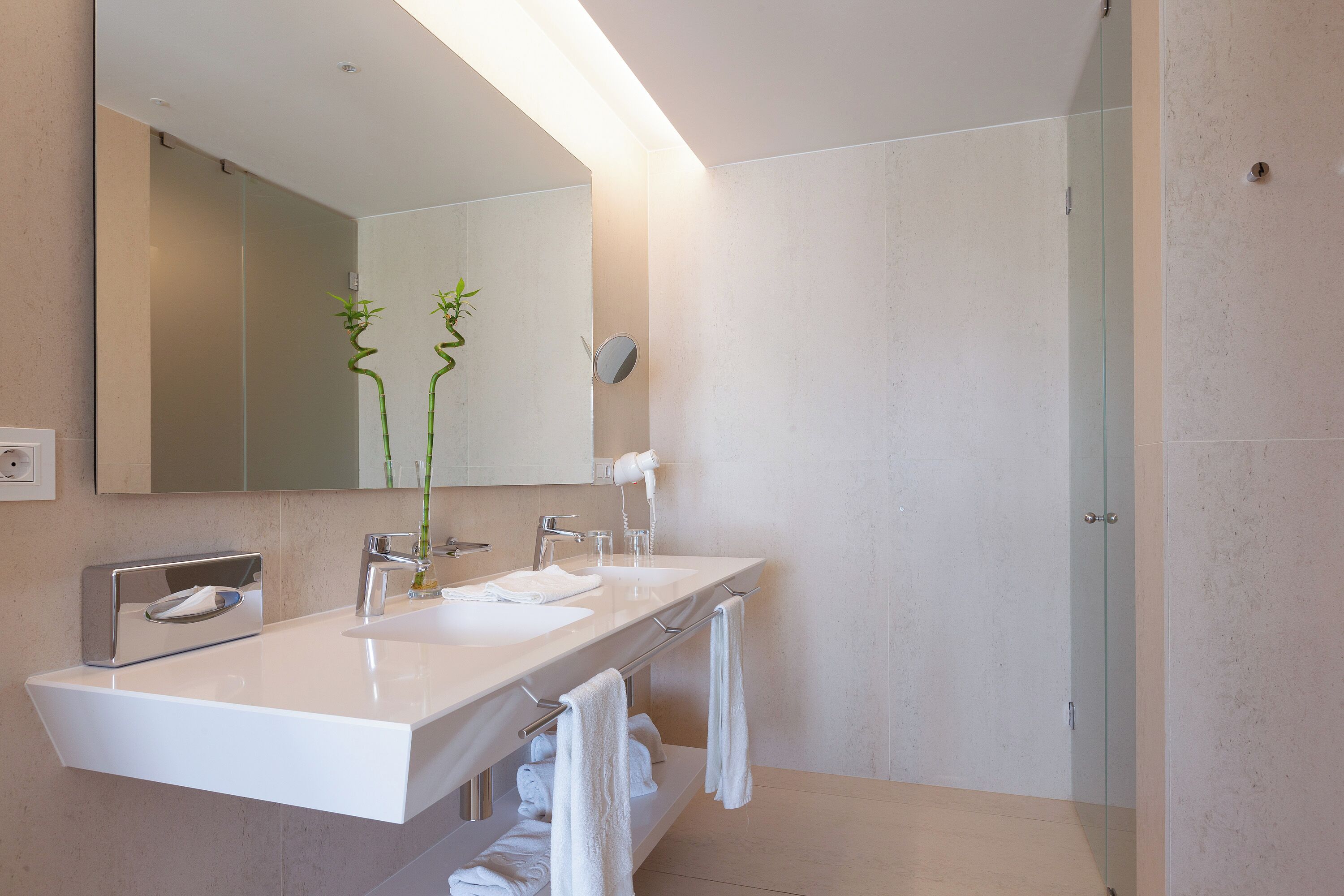 A modern bathroom with a large mirror, two sinks, and a glass shower enclosure.