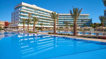 A hotel with a large swimming pool, palm trees, and sun loungers.