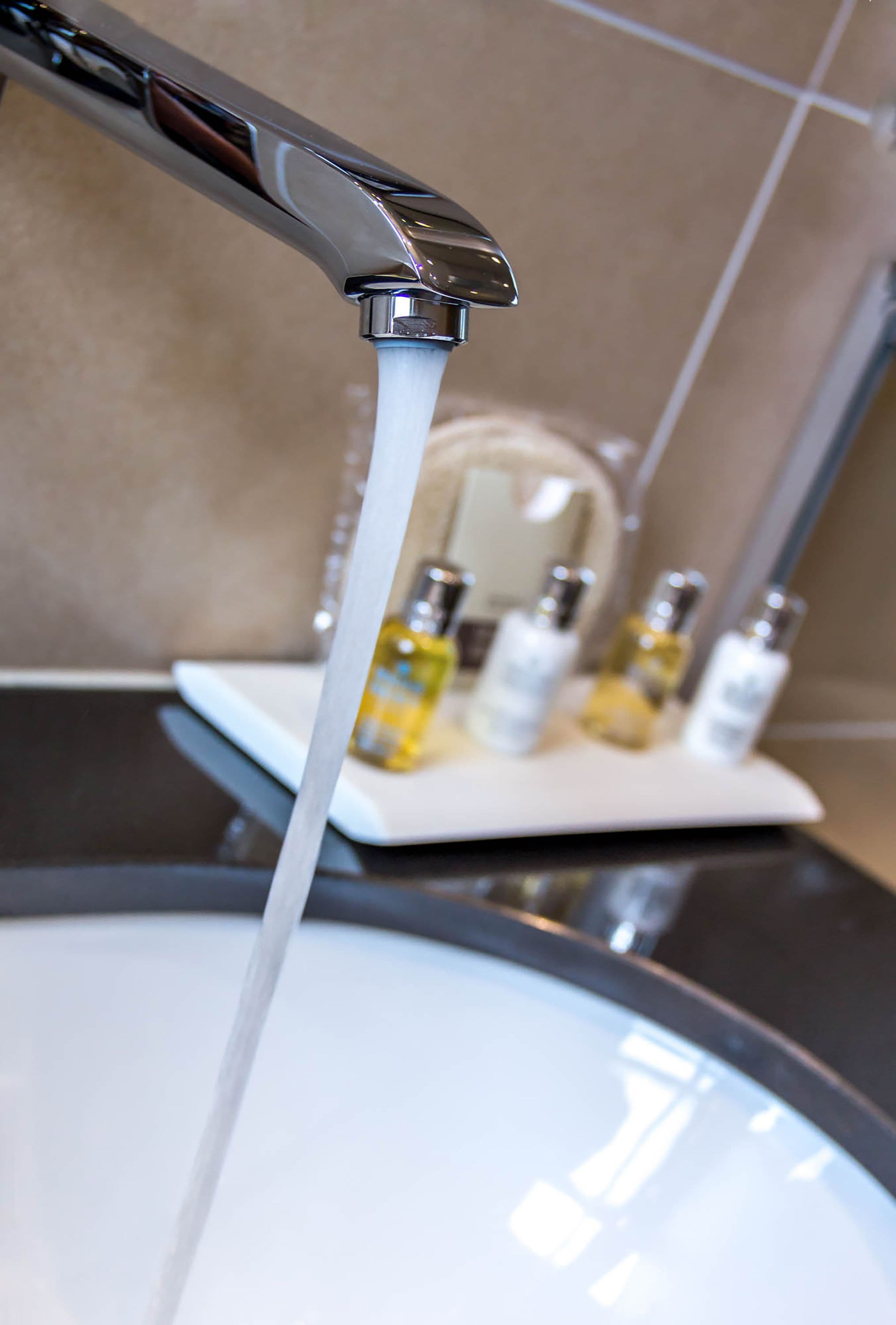 A bathroom sink with running water, a mirror, and several bottles of toiletries on the counter.