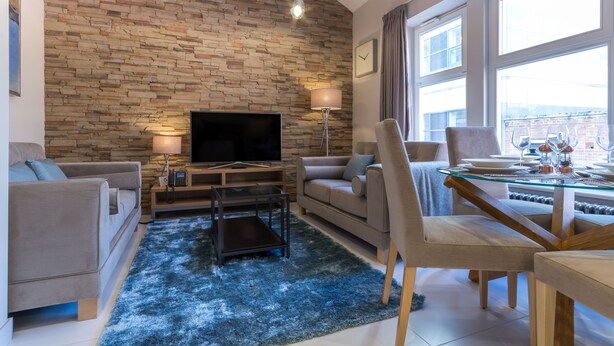 Una sala de estar moderna con una pared de piedra, un televisor de pantalla plana, una mesa de comedor de vidrio y un sofá acogedor.