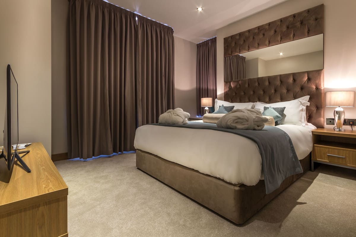 A modern hotel room with a large bed, a wooden desk, a flat-screen TV, and a large mirror above the bed.