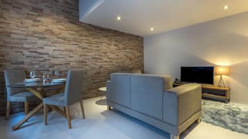 Ein modernes Wohnzimmer mit Steinwand, Glastisch, grauem Sofa und Fernseher auf einem Holzboden.
