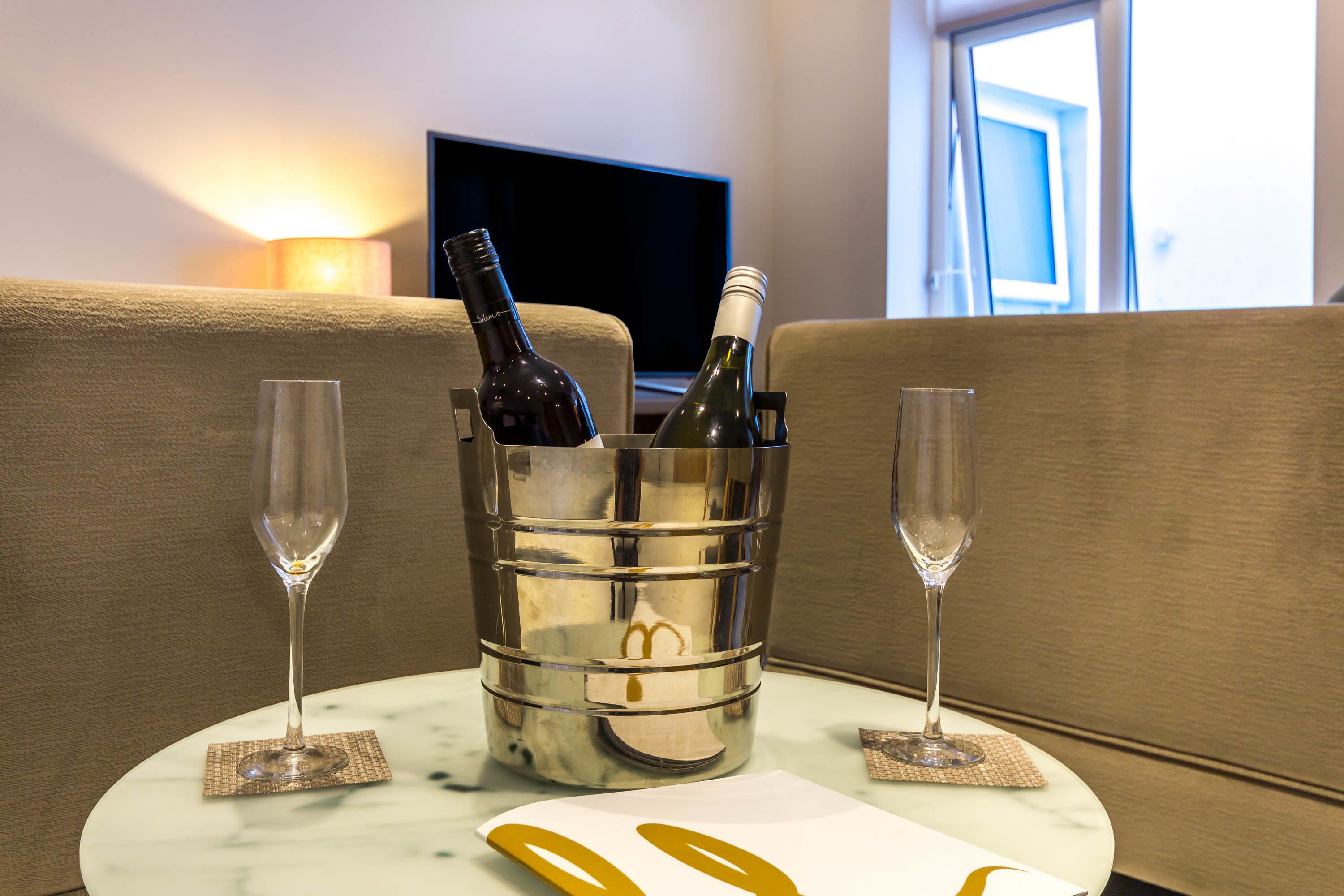 Una habitación con un sofá, televisión y una mesa con una botella de vino y dos copas.