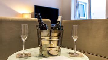 Una habitación con un sofá, televisión y una mesa con una botella de vino y dos copas.