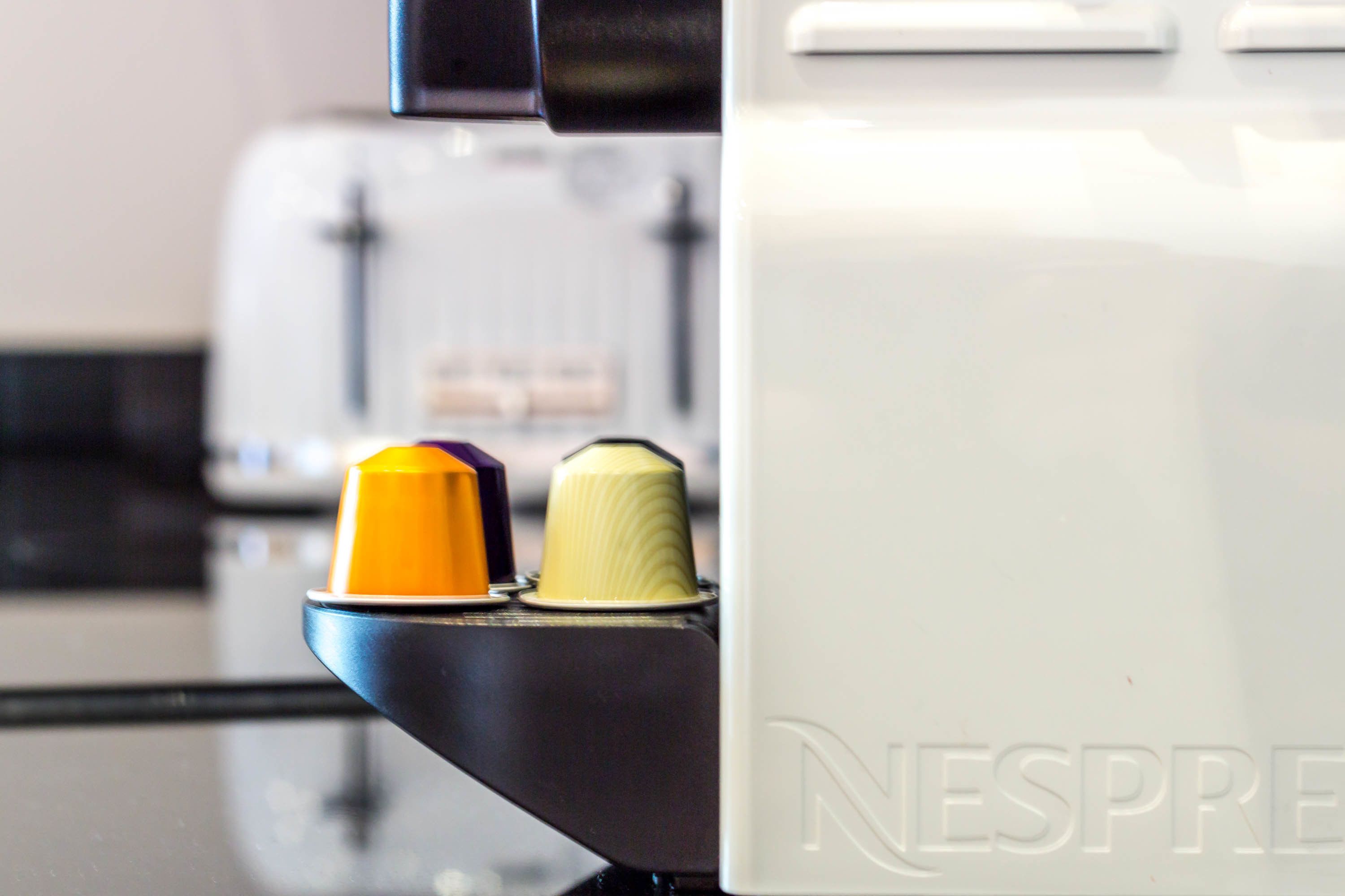 Een koffieapparaat met een Nespresso logo, een gele en een witte capsule, en een zwart opvangbakje.