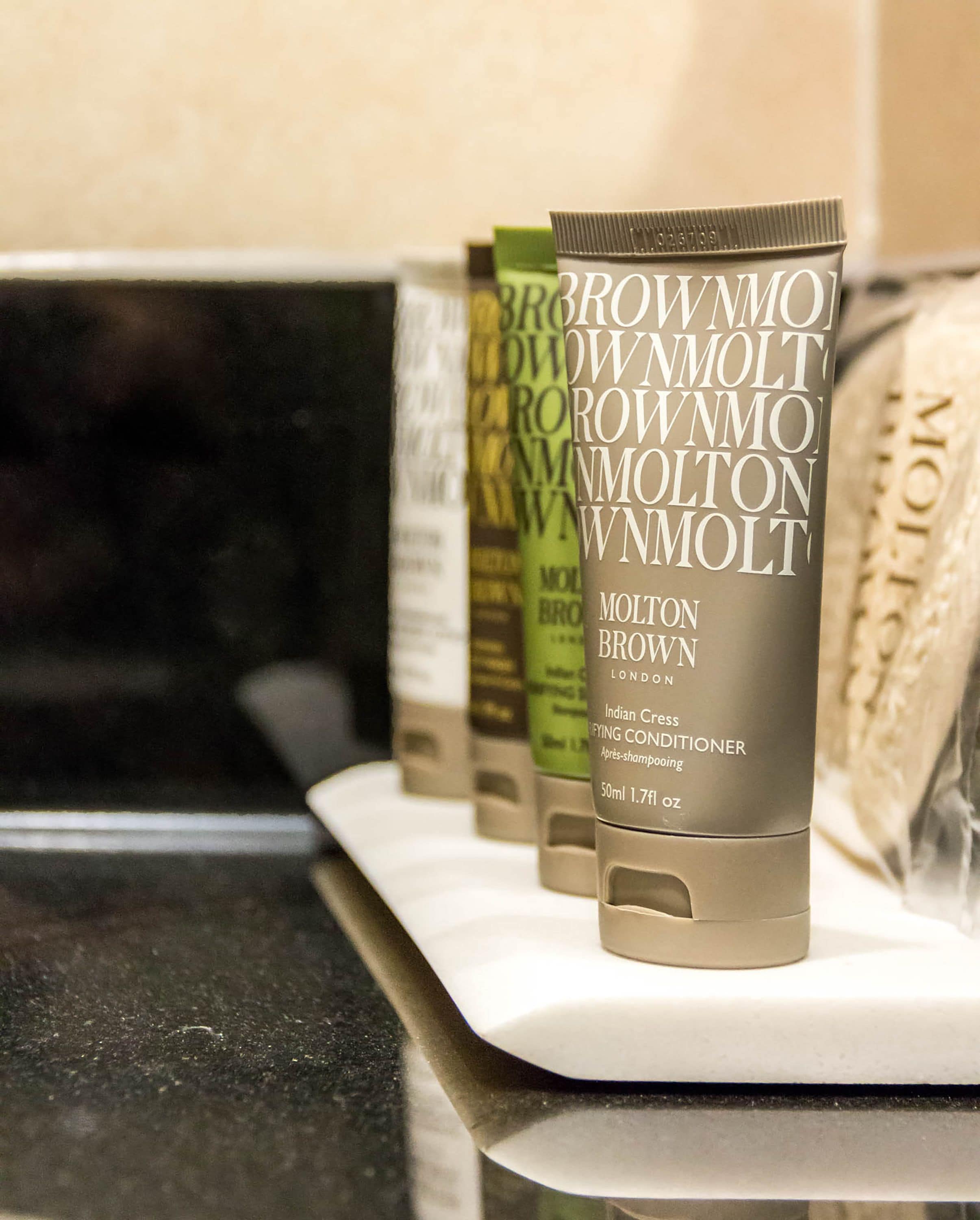 Une rangée de tubes de crème de soin pour cheveux « Indian Crest » de la marque Molton Brown, alignés sur une étagère.