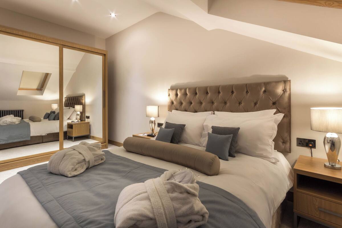 A hotel room with a large bed, a mirror, a nightstand, and a lamp.